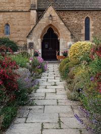 Image of cottage garden path leading up to a church entry with a small deer standing next to the gated arch