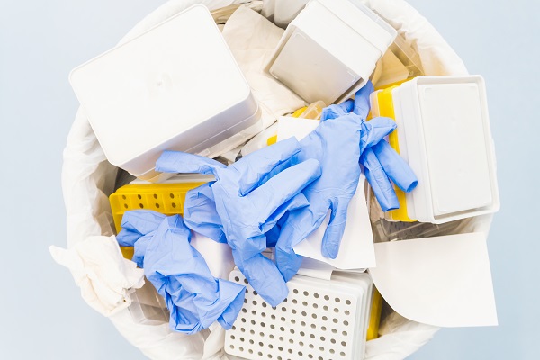 Birdseye photo of blue gloves and other lab waste in a bin, blue background